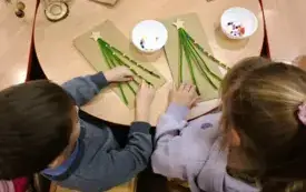 Dzieci dekorują choinkę koralikami.