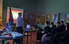 Z  lewej strony stoi piękna choinka. Obok na stole leżą przedmioty związane z Francją. Po prawej młodzież siedzi na krzesłach. Przed nimi ekran z prezentacją.
