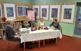 Cztery  Klubowiczki siedzą. Na stole leżą książki. Na stole jest wystawiony poczęstunek.