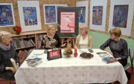 Cztery czytelniczki siedzą przy stole. Rozmawiają o książce. Na stole jest biały obrus. Za nimi wiszą kolorowe prace świąteczne.
