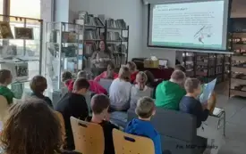 Uczestnicy siedzą na krzesłach przed ekranem z prezentacją.