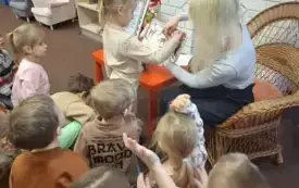 Dziecko otwiera okienko w książce trzymanej przez bibliotekarkę.