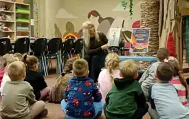Bibliotekarka czyta dzieciom książkę, a przedszkolaki słuchają z zainteresowaniem.