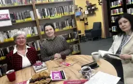 Klubowicze w rozmowie na temat książki, w tle regały na książki, oraz logo DKK.