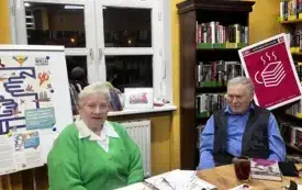 Klubowicze w rozmowie na temat książki, w tle regały na książki, oraz logo DKK.
