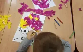 Dzieci wykonują fryzurę babci z bibuły, przyklejając kawałki bibuły do ilustracji.