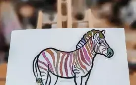Kolorowa zebra wykonana z papieru. W tle dzieci malujące własne zebry.