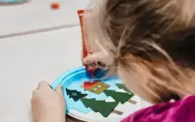 Dziewczynka przykleja klejem elementy do pracy plastycznej.