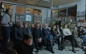 Grupa os&oacute;b siedzi na krzesełkach.