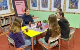 Cztery nastolatki siedzą przy stole z moderatorką, piją herbatę i rozmawiają o książce.