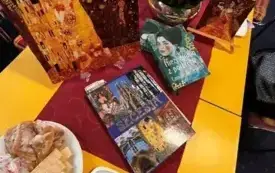 St&oacute;ł przygotowany na spotkanie DKK z kwiatami w doniczce, książkami, ozdobnymi talerzami z obrazami Gustava Klimta i słodyczami