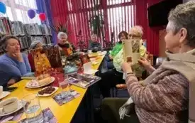 Siedem kobiet siedzi przy stole podczas spotkania DKK, jedna z uczestniczek prezentuje ciekawe zdjęcia