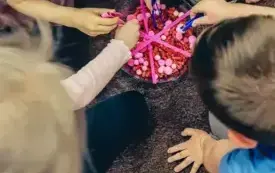 Dzieci wyciągają pęsetami serduszka z kolorowych pompon&oacute;w i makaronu.