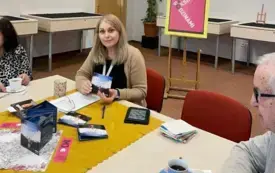 Kobieta siedzi przy stole, w ręku opakowanie od audiobooka.