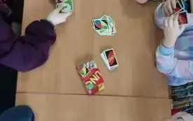 Na jasno-brązowym blacie karty gry UNO. Ręce dzieci trzymające karty.