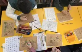 Grupa przy stole koloruje mapy kredkami
