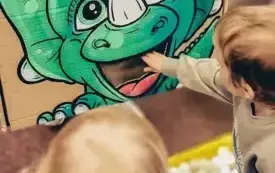 Chłopcy karmią dinozaura piłeczkami pingpongowymi.