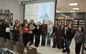 Kobieta siedzi przy stole podpisując książkę.