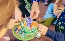 Bibliotekarka rozdaje dzieciom papierowe dinozaury.