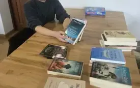 Mężczyzna siedzi przy stole i prezentuje wybrane przez siebie książki.