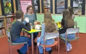 Cztery nastolatki siedzą z moderatorką przy stole. W tle wisi wystawa fotografii. 