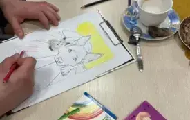 Na stole leży opakowanie audiobooka, filiżanka, kredki, malowanka, dłonie.