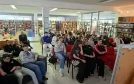Osoby siedzące na krzesłach w pomieszczeniu biblioteki.