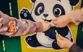Dzieci karmią pandę bambusem ze słomek.