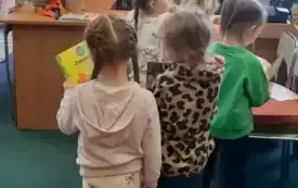 Dzieci stoją w rządku przed biurkiem bibliotekarki i czekają na swoją kolej, żeby wypożyczyć książeczki.