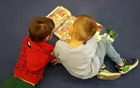 Dw&oacute;ch chłopc&oacute;w na dywanie ogląda komiks.