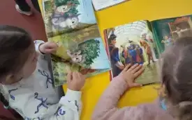 Dwie dziewczynki przy ż&oacute;łtym stoliku ogląda bajeczki.