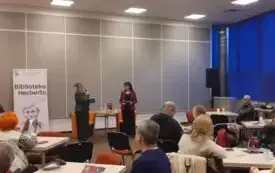 Agnieszka Kopaczyńska-Moskaluk oraz Beata Igielska stoją przed publicznością i przemawiają do mikrofonu.