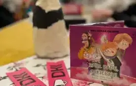 Na stole stoi opakowanie audiobooka, figurka kota, w tle siedzi młodzież.