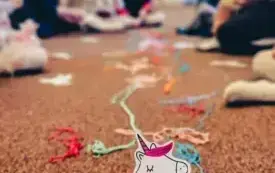 Jednorożec z kolorową grzywą z wł&oacute;czki. W tle dzieci wykonujący zadanie.