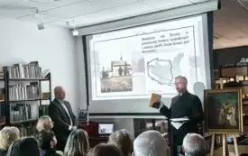 Osoba stoi przed ekranem. W tle osoby siedzące na krzesłach.