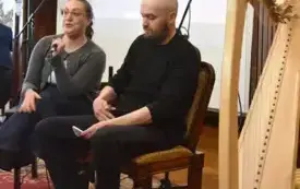 Mężczyzna i kobieta siedzą obok siebie, koło nich stoi hatfa