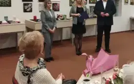 Przed publicznością stoją trzy osoby i przemawiają do gości