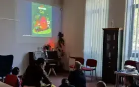 Uczniowie i nauczycielki oglądają okładkę książki, bibliotekarka czyta opowieść