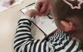Dziewczynka siedzi przy stoliku. Dziewczynka przesuwa koraliki umiesczone wewnątrz rękawiczki.