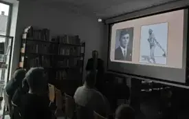Mężczyzna stoi przy ekranie naprzeciwko siedzących ludzi - mniejszy kadr