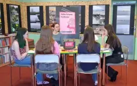 Pięć uczestniczek spotkania wraz z moderatorką siedzą przy stole i rozmawiają o książce. Za nimi stoi sztaluga z plakatem DKK.