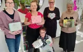 Pięć uczestniczek zajęć stoi przy lustrach, na kt&oacute;re &bdquo;spływa&rdquo; roślinność. Każda z nich trzyma ozdobioną przez siebie pracę na warsztatach decoupage &bdquo;Pamiątki w stylu vintage&rdquo;. W tle opr&oacute;cz luster widać komodę z książkami, białe drzwi, białą ścianę, tablic