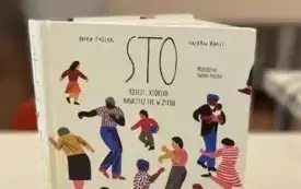 Książka stoi na stole, przed nią rozrzucone kolorowe kredki.