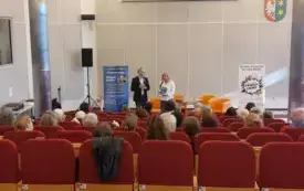 Przed publicznością siedzącą na czerwonych krzesłach stoją i przemawiają Tomasz Terefenko oraz Agnieszka Przybył.
