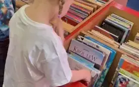 Dziewczynka przegląda książeczki dla najmłodszych znajdujące się w czerwonym kasetonie.