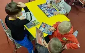 Czterech chłopc&oacute;w przy stoliku ogląda książeczki.