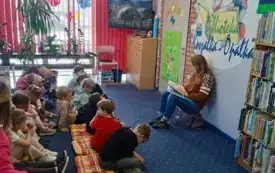 Kobieta siedząca przed grupą dzieci czyta im bajkę