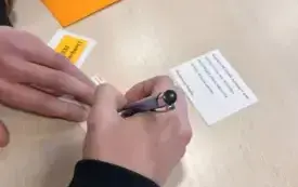Widoczna dloń z długopisem, obok koperta i kartka papieru