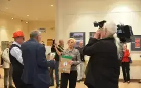 Goście na wernisażu rozmwaiają. Obok kamerzysta z kamerą i fotograf z aparatem.