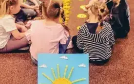 Dzieci siedzą w grupie i przeplatają druciki, tworząc słoneczka.